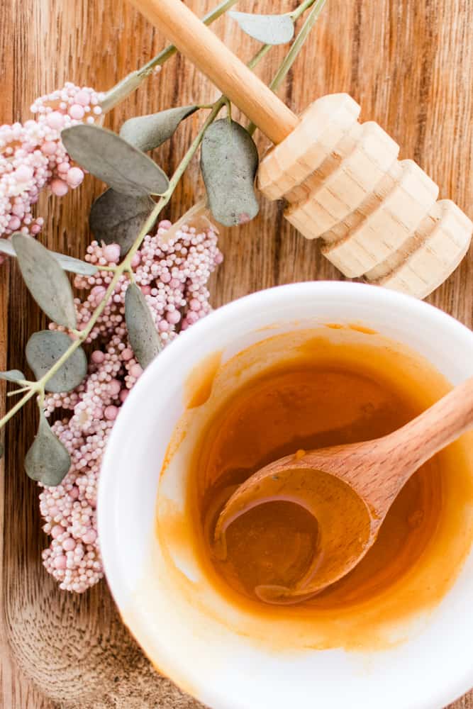 Homemade honey face mask being stirred in with a wooden spoon on a wooden table.