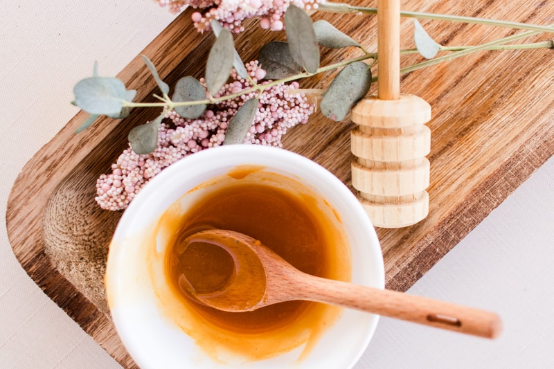 Face mask with honey for glowing skin on a wooden cutting board with dried springs and a honey comb.