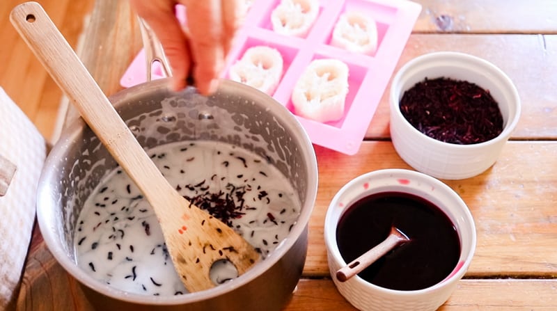 Stirring in dried hibiscus flowers and essential oils into the soap base.