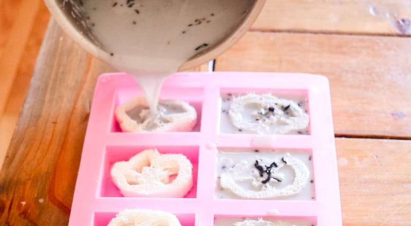 Pouring recently melted soap into molds with the loofah to make exfoliating soap bars.