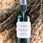 Hair detangler spray in a green glass spray bottle in a wicker mat resting on dried lavender sprigs.