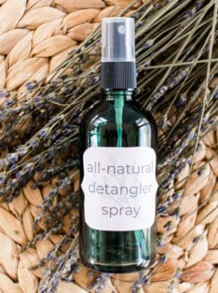 Hair detangler spray in a green glass spray bottle in a wicker mat resting on dried lavender sprigs.