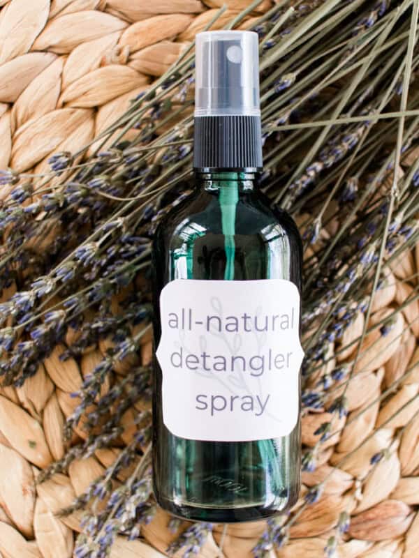 Hair detangler spray in a green glass spray bottle in a wicker mat resting on dried lavender sprigs.