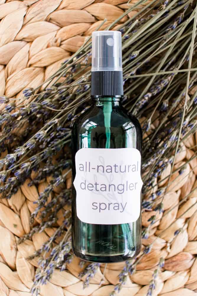 Hair detangler spray in a green glass spray bottle in a wicker mat resting on dried lavender sprigs.