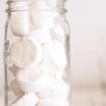 DIY dishwasher detergent pods in an airtight storage container on wooden shiplap laundry table.