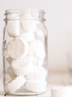 DIY dishwasher detergent pods in an airtight storage container on wooden shiplap laundry table.