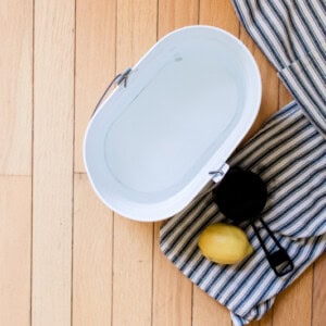 Homemade wood floor cleaner in a mop bucket with a cleaning towel and a lemon.