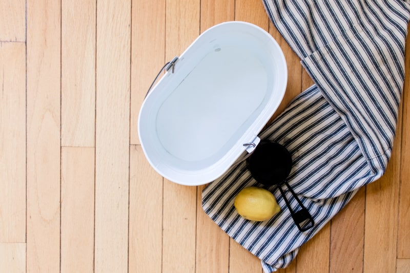 Homemade wood floor cleaner in a mop bucket with a cleaning towel and a lemon.