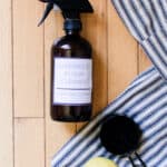 Hardwood floor cleaner diy spray with a label, towel, lemon and measuring cup on hardwood floor.