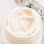Natural homemade night cream in a shallow glass jar with flowers on white marble.