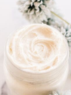 Natural homemade night cream in a shallow glass jar with flowers on white marble.