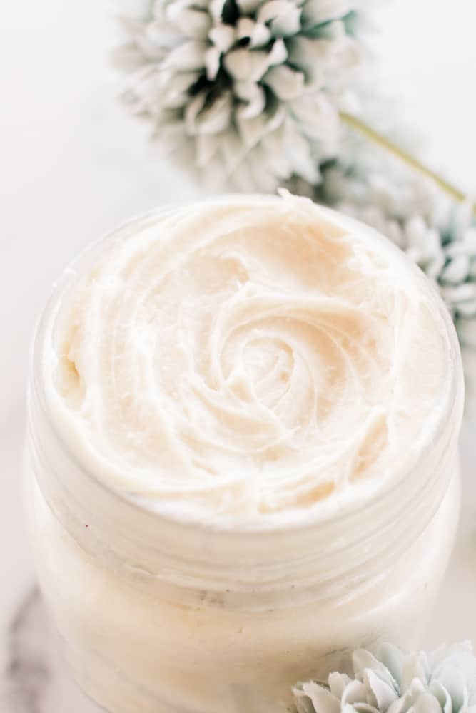 Natural homemade night cream in a shallow glass jar with flowers on white marble.