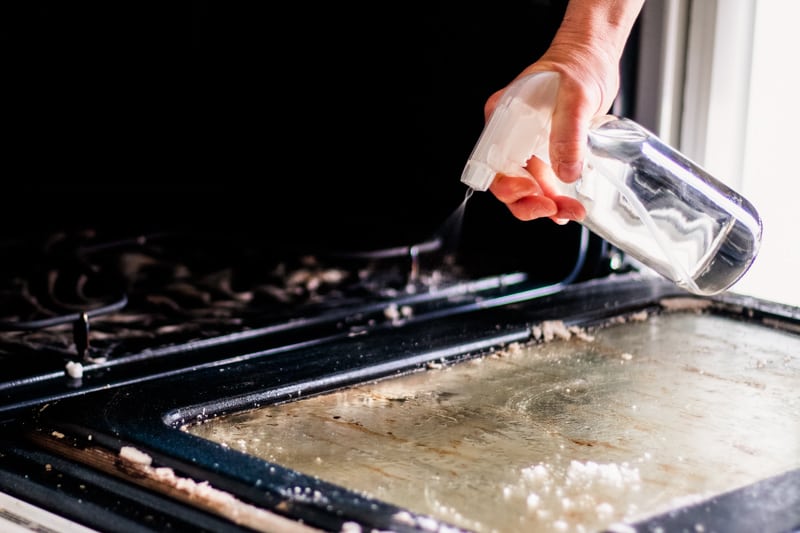 Spraying a degreaser on the oven door to clean it.