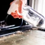Homemade oven cleaner being sprayed onto oven door glass.