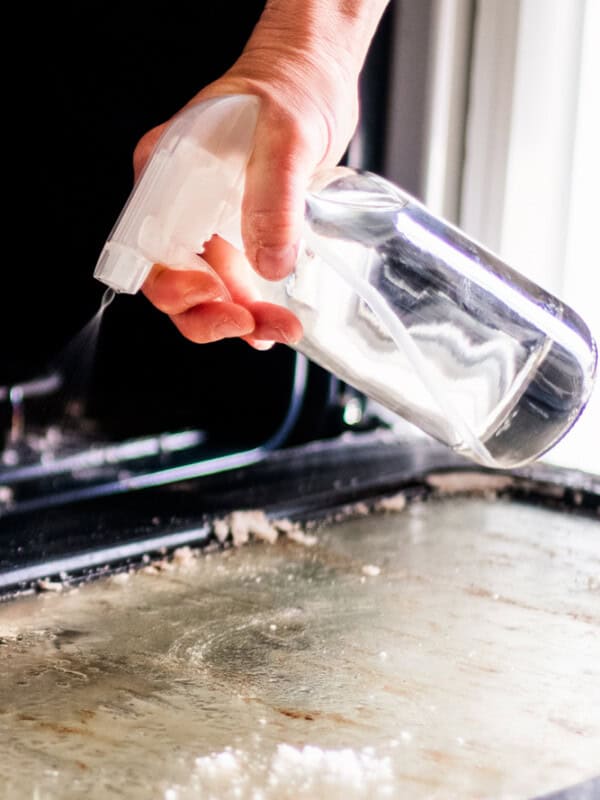 Homemade oven cleaner being sprayed onto oven door glass.