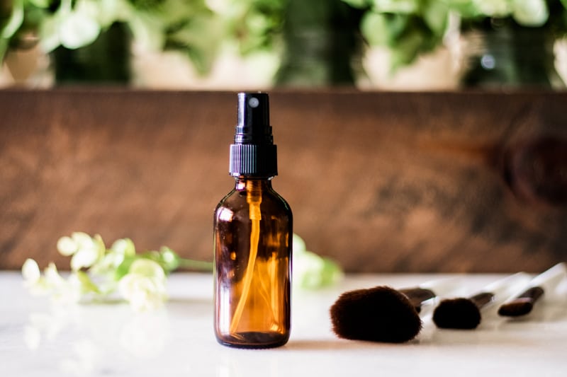 Homemade makeup setting spray for dry skin with flower pedals and wooden background.