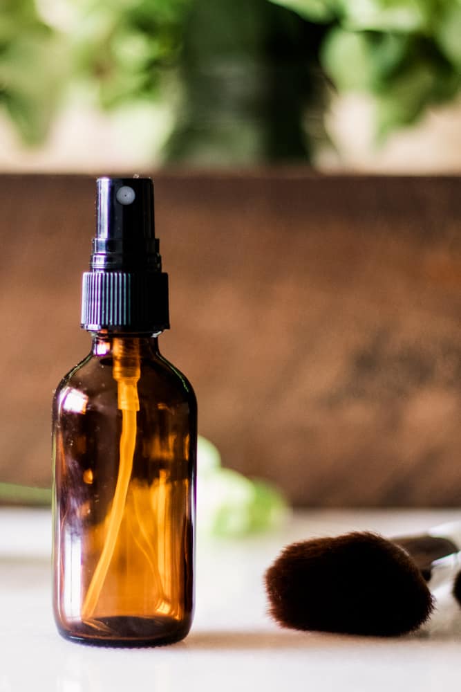 DIY setting spray for makeup with mist nozzle on a white vanity with a wooden backdrop.