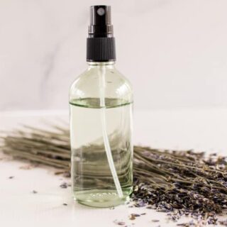DIY body spray naturally scented in a glass spray bottle surrounded by lavender springs on a white vanity.