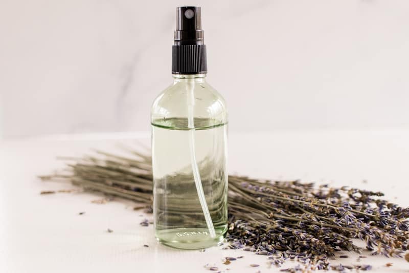 DIY body spray naturally scented in a glass spray bottle surrounded by lavender springs on a white vanity.