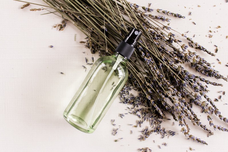 Homemade body spray perfume lying on white marble with dried lavender leaves.