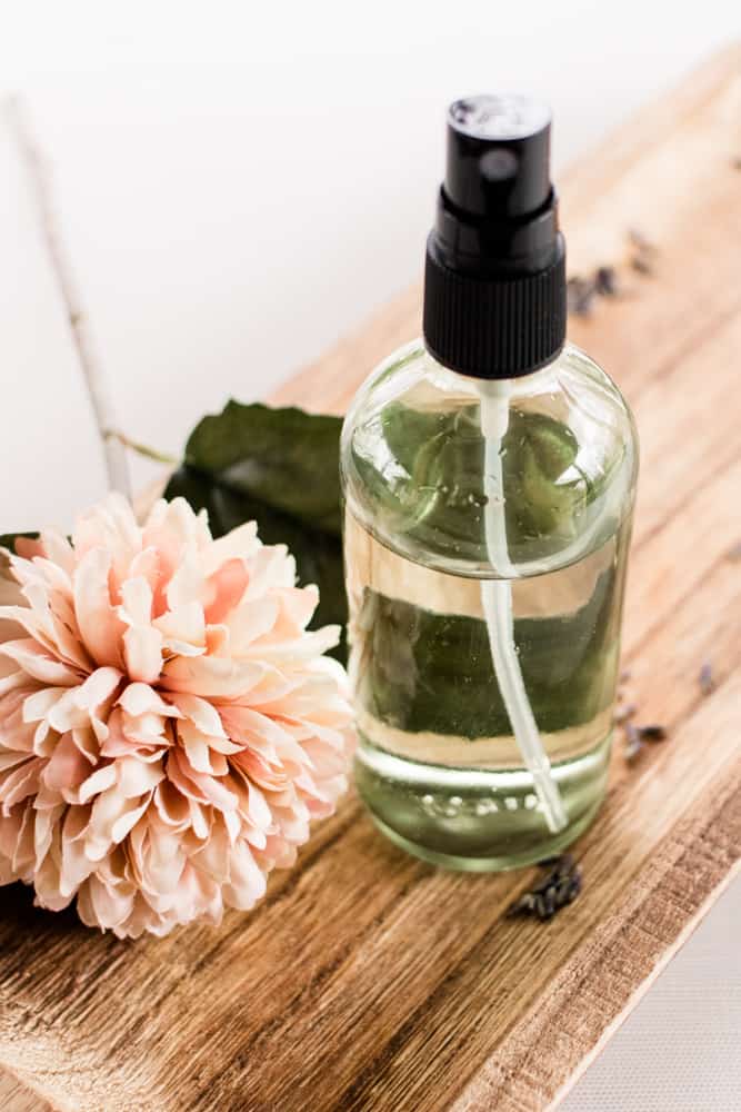 Essential oil spray perfume on wooden top with a large pink flower.