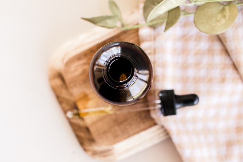 Carrier oil in a glass jar with a dropper top on white counter with a checkered tea towel and green plant.