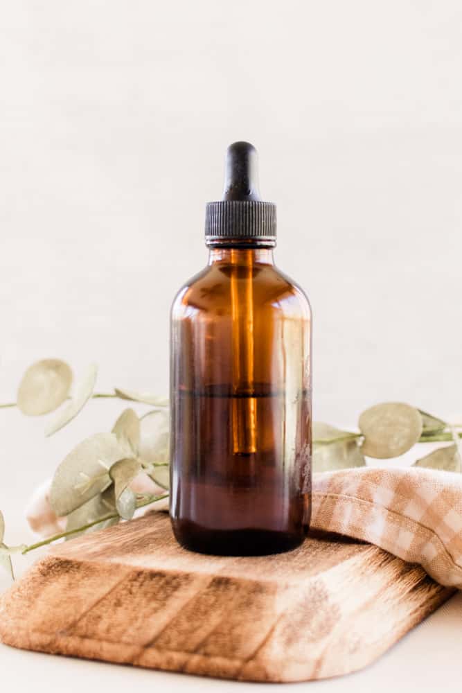 Glass carrier oil bottle with a jojoba plant in the background.