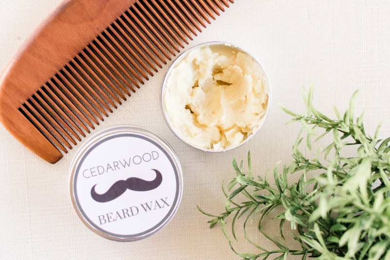 Cedarwood beard wax and wooden comb on white table.