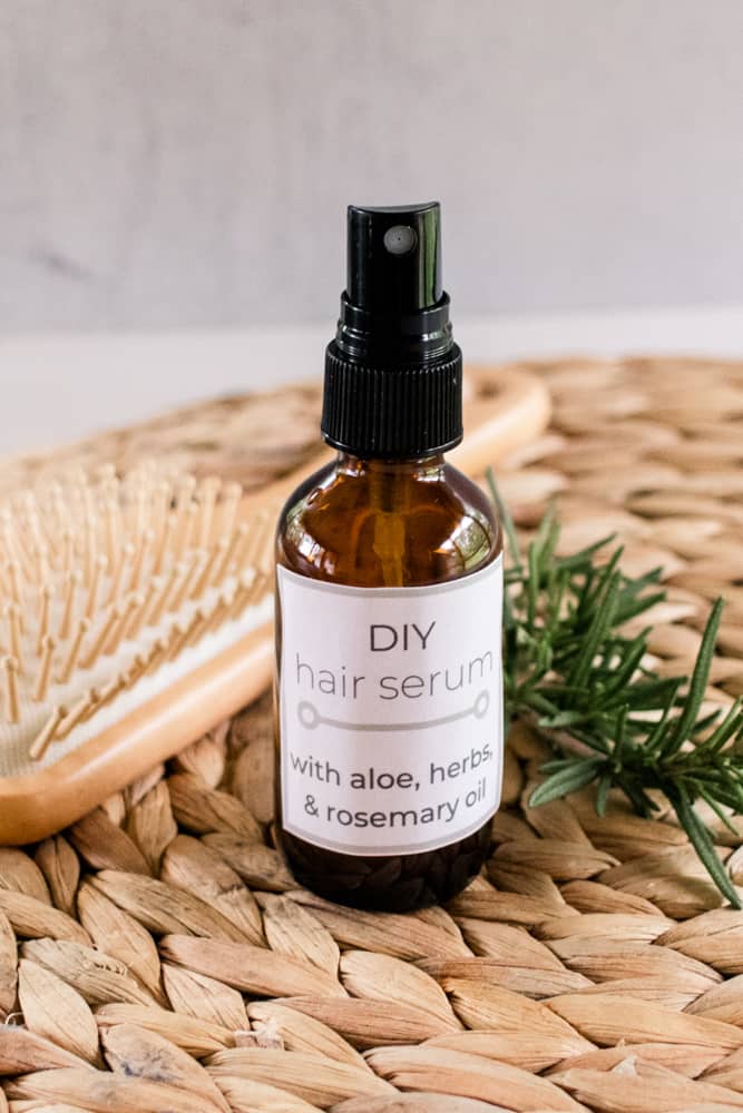 DIY hair serum in an amber colored glass bottle on a wicker mat with dried nettle and a hair comb.