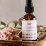 Natural diy hair serum in a glass mist bottle on a wooden makeup tray with dried flowers.