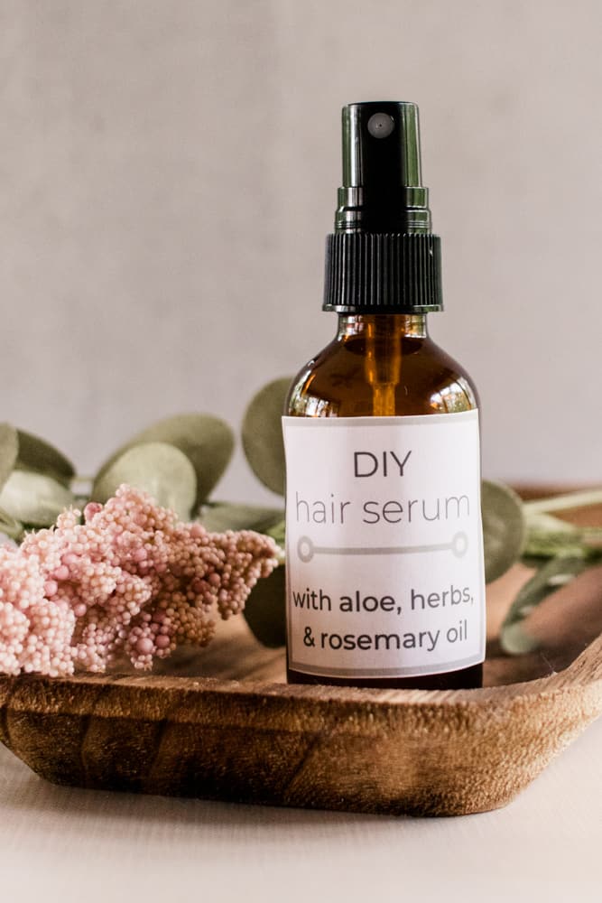 Natural diy hair serum in a glass mist bottle on a wooden makeup tray with dried flowers.