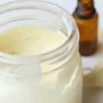 Homemade sunscreen on white table with hunks of cocoa butter next to it.