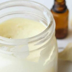 Homemade sunscreen on white table with hunks of cocoa butter next to it.