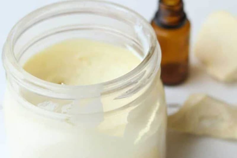 Homemade natural sunscreen recipe on white table with hunks of cocoa butter next to it.