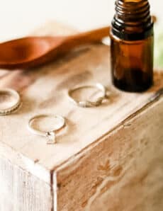 Homemade jewelry cleaner with 3 rings, and a wooden spoon on a wooden jewelry box.