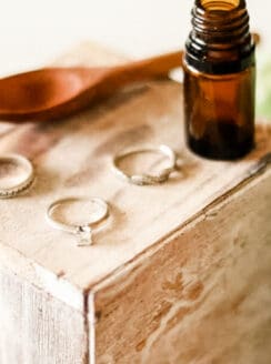 Homemade jewelry cleaner with 3 rings, and a wooden spoon on a wooden jewelry box.