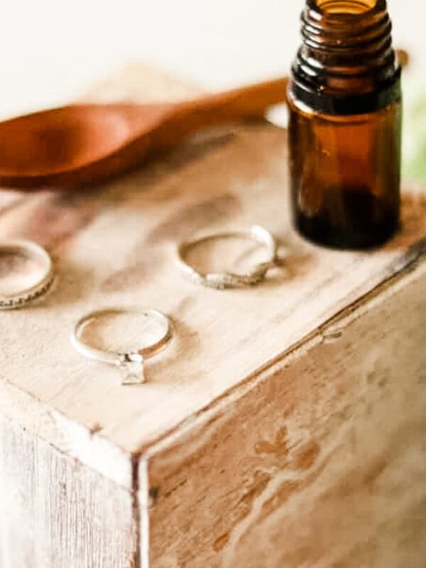 Homemade jewelry cleaner with 3 rings, and a wooden spoon on a wooden jewelry box.