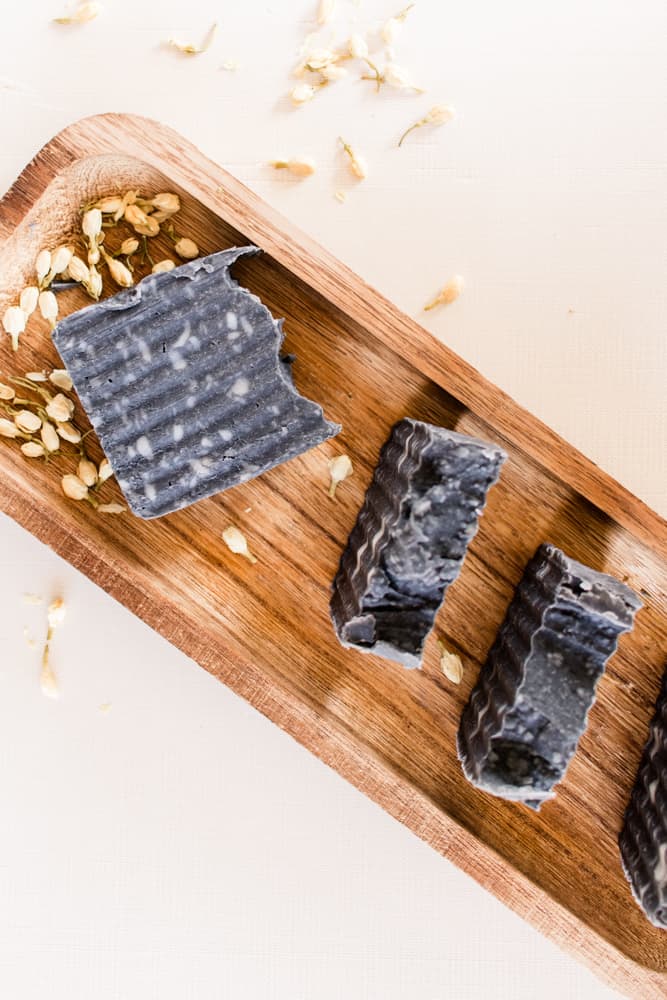 Homemade charcoal soap bars with ragged tops on wooden drying board.