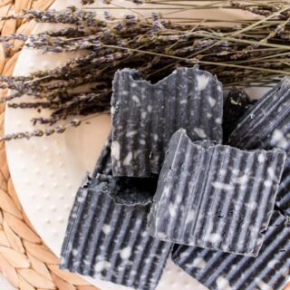 Homemade activated charcoal soap bars with riveted sides, dried lavender on a white plate.