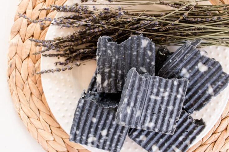 Homemade activated charcoal soap bars with riveted sides, dried lavender on a white plate.