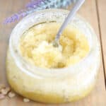 Homemade sugar scrub with olive oil in a glass container on wooden shiplap.