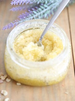 Homemade sugar scrub with olive oil in a glass container on wooden shiplap.