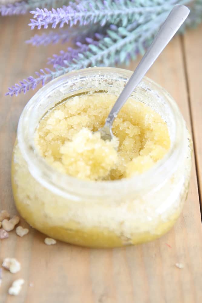 Homemade sugar scrub with olive oil in a glass container on wooden shiplap.