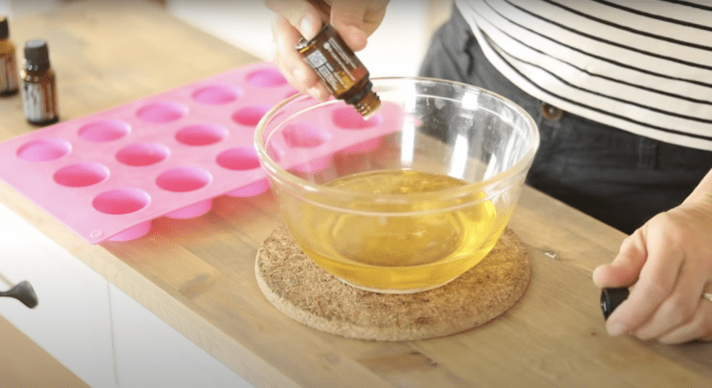 Adding essential oils into a glass bowl filled with melted ingredients