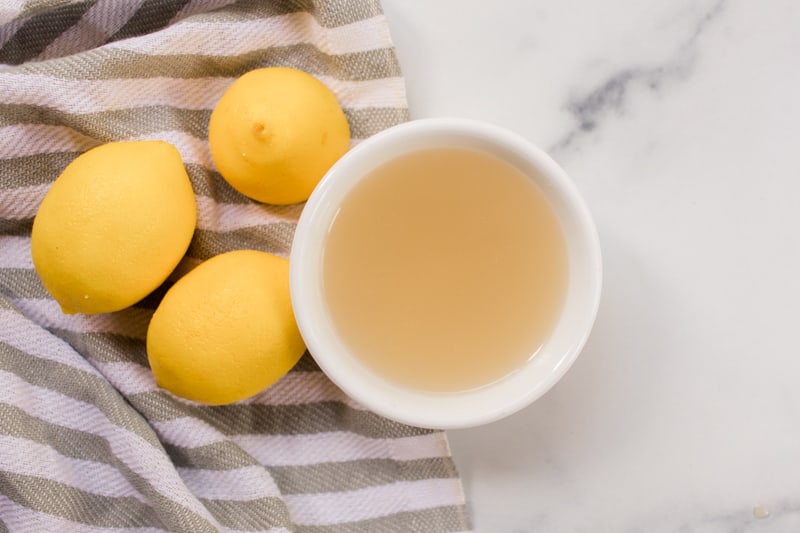 Lemon juice hair lightener in a small white bowl with 3 lemons.