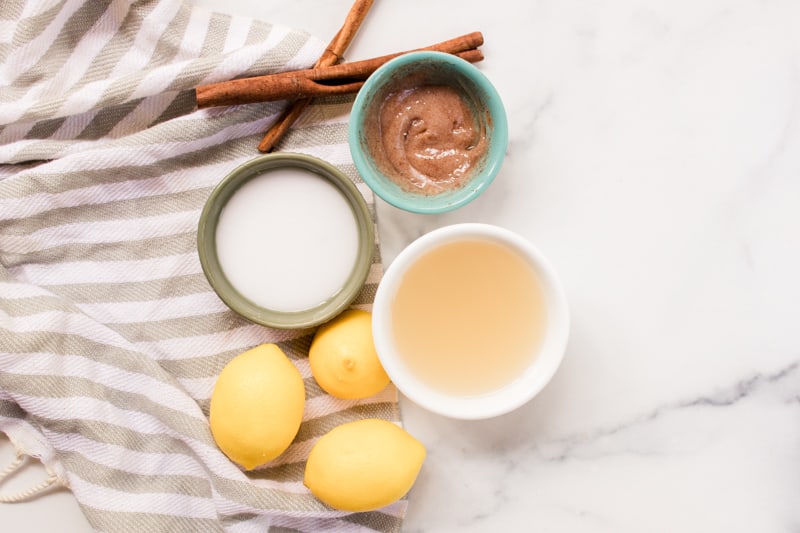 Three bowls of hair lighteners with fresh lemons and cinnamon sticks on white marble.