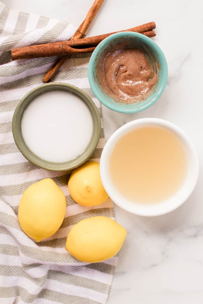 Natural hair lighteners in different colored bowls with cinnamon sticks, lemons and grey and white striped towel.