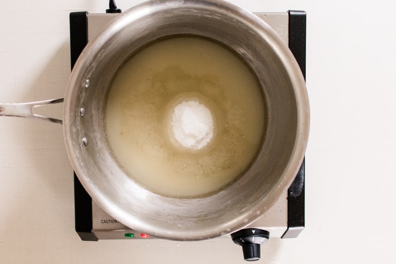 Sugar wax ingredients in a small saucepan being melted on a countertop range.