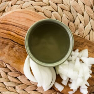 Homemade onion oil cooling in a small green bowl on a wooden cooling board.