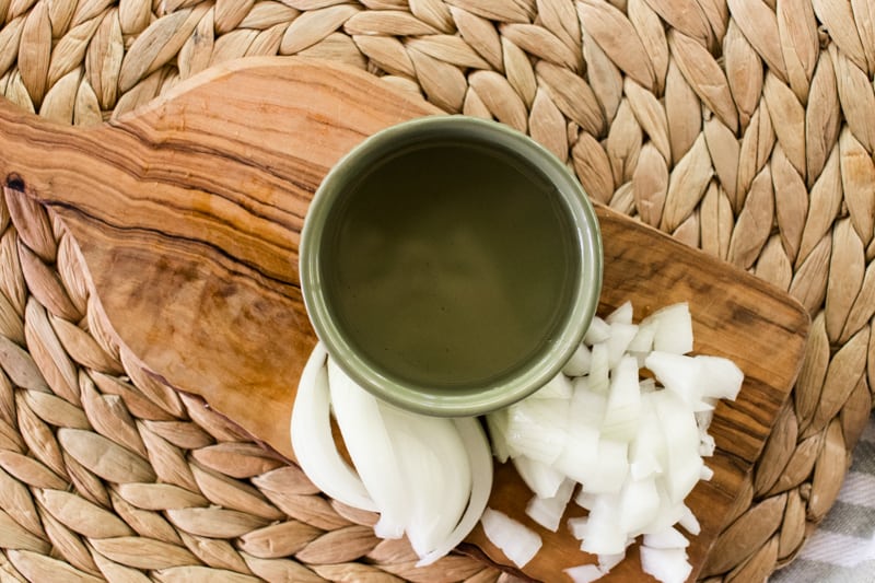 Homemade onion oil cooling in a small green bowl on a wooden cooling board.